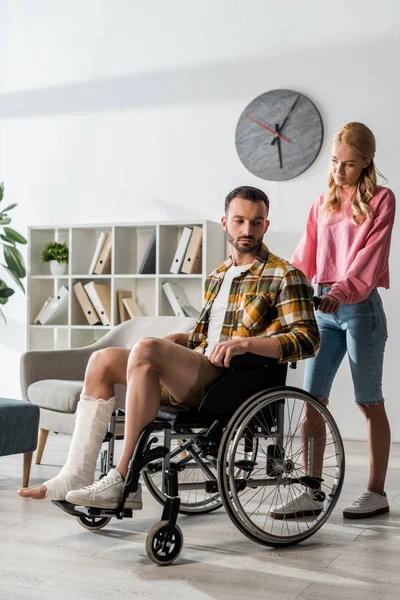 Привлекательная женщина, стоящая возле бородатого мужчины, сидящего в инвалидном кресле — стоковое фото