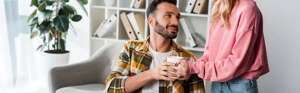 Tiro panorâmico de mulher dando xícara de chá ao homem barbudo — Fotografia de Stock