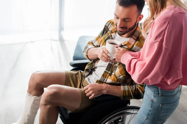 Happy bearded man sitting in wheelchair and taking cup with tea — Stock Photo