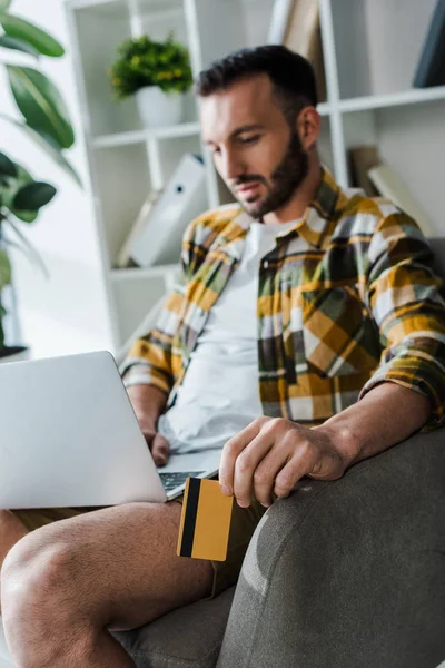 Вибірковий фокус бородатого чоловіка, який тримає кредитну картку під час онлайн-покупки вдома — стокове фото