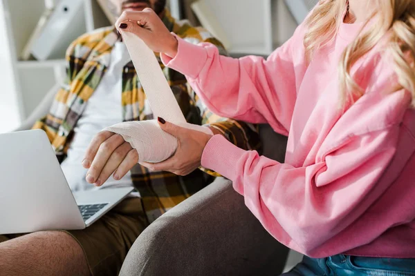 Cropped view of caring woman putting bandage on injured arm of bearded man — Stock Photo