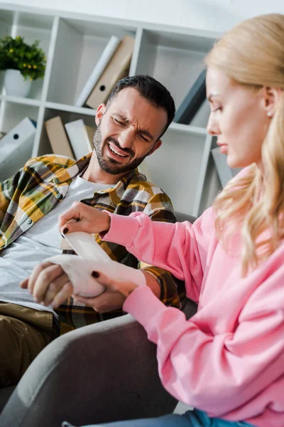 Selective focus of caring woman putting bandage on injured hand of bearded man — Stock Photo