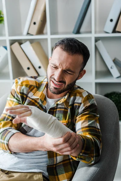 Verletzter bärtiger Mann blickt auf Hand in Verband — Stockfoto