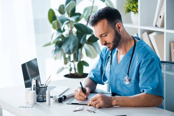 Schöner bärtiger Arzt schreibt Diagnose in Klinik — Stockfoto