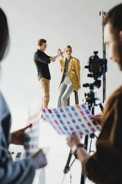 Foco seletivo do cabeleireiro fazendo penteado ao modelo elegante e produtor com fotógrafo nos bastidores — Fotografia de Stock