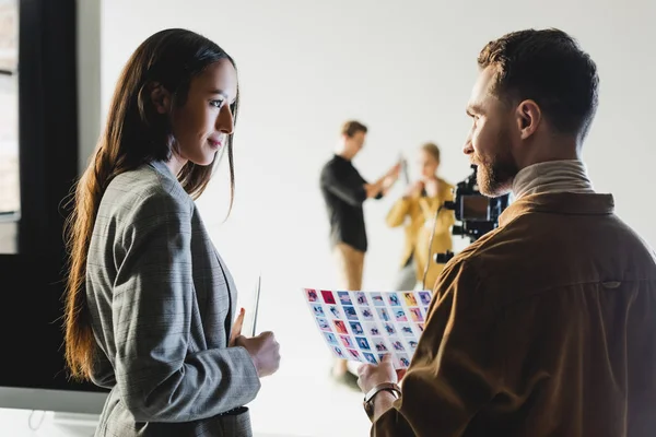 Selective focus of producer with photographer talking on backstage and hairstylist with model on background — Stock Photo