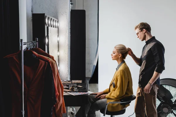 Vista laterale di parrucchiere facendo acconciatura a modello elegante sul backstage — Foto stock
