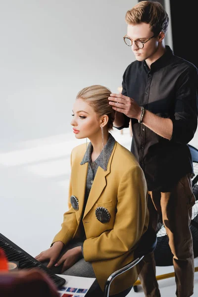 Cabeleireiro bonito fazendo penteado ao modelo elegante nos bastidores — Fotografia de Stock