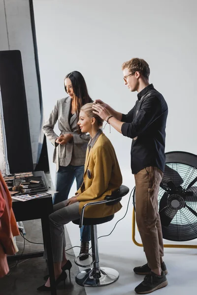 Cabeleireiro fazendo penteado e modelo com produtor olhando para longe nos bastidores — Fotografia de Stock