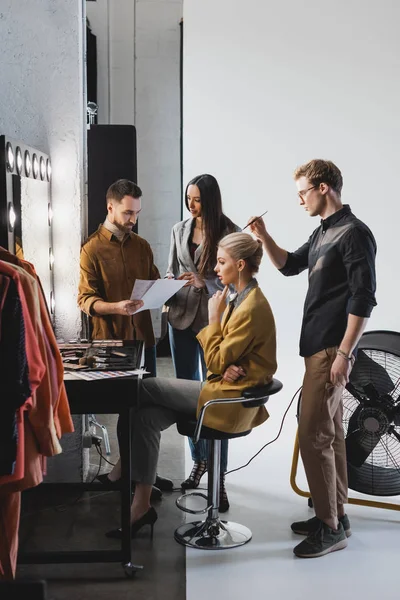 Produtor e fotógrafo falando e cabeleireiro fazendo penteado ao modelo elegante nos bastidores — Fotografia de Stock