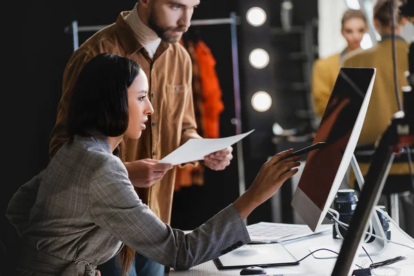 Mise au point sélective du producteur pointant vers l'ordinateur et le photographe en le regardant dans les coulisses — Photo de stock