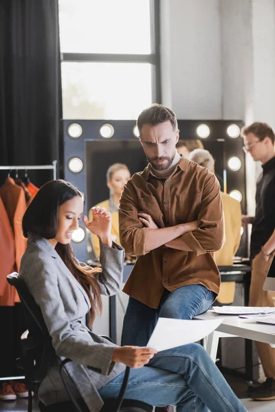 Messa a fuoco selettiva del produttore e fotografo arrabbiato guardando la carta sul backstage — Foto stock