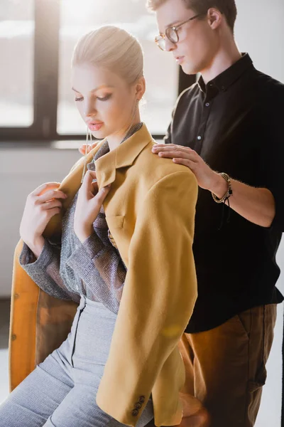 Estilista bonito vestindo jaqueta no modelo elegante nos bastidores — Fotografia de Stock