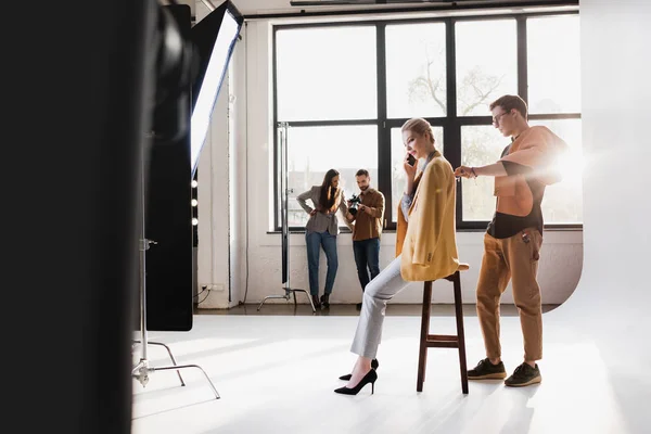 Stilista utilizzando rullo di lanugine, modello parlando su smartphone, produttore e fotografo parlando sul backstage — Foto stock