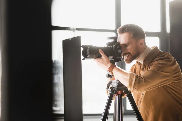 Selective focus of smiling photographer taking photo with digital camera on backstage — Stock Photo