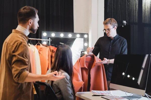 Enfoque selectivo de estilista apuntando con la mano y mostrando chaqueta al productor y fotógrafo en el backstage - foto de stock
