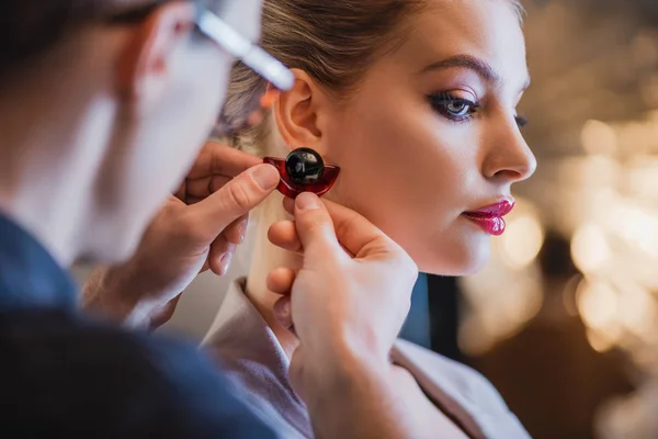 Cropped view of stylist putting earring on model on backstage — Stock Photo