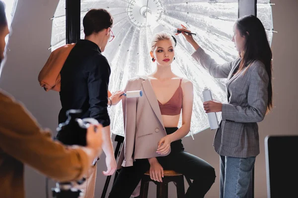 Foco seletivo do estilista usando rolo de fiapos e cabeleireiro fazendo penteado ao modelo elegante nos bastidores — Fotografia de Stock