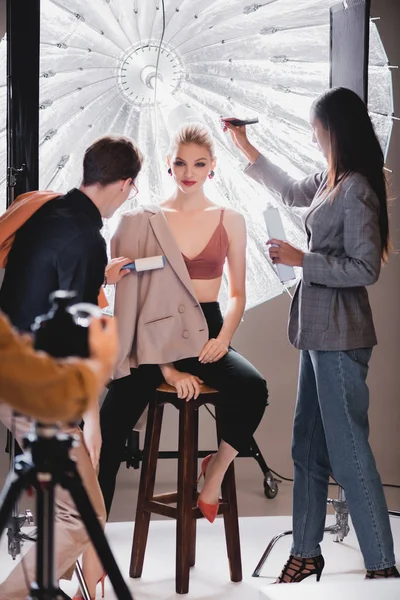 Foco seletivo do estilista usando rolo de fiapos e cabeleireiro fazendo penteado ao modelo elegante nos bastidores — Fotografia de Stock