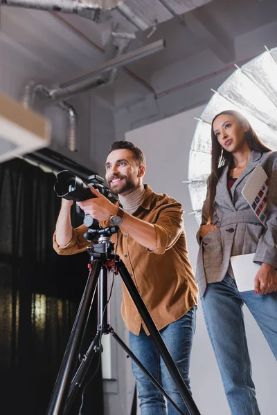 Low angle view of smiling photographer taking photo and producer looking away on backstage — Stock Photo
