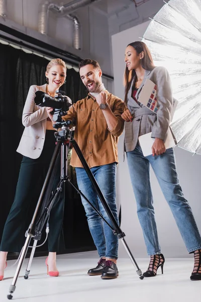 Niedrigwinkelaufnahme lächelnder Fotograf, Model und Produzent beim Betrachten der Digitalkamera hinter der Bühne — Stockfoto
