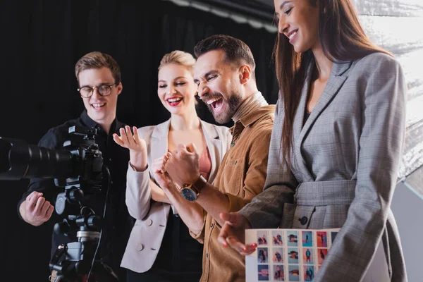 Photographe souriant, modèle, styliste et producteur regardant l'appareil photo numérique dans les coulisses — Photo de stock