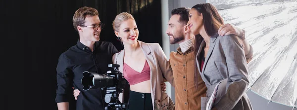 Panoramic shot of smiling photographer, model, stylist and producer hugging on backstage — Stock Photo