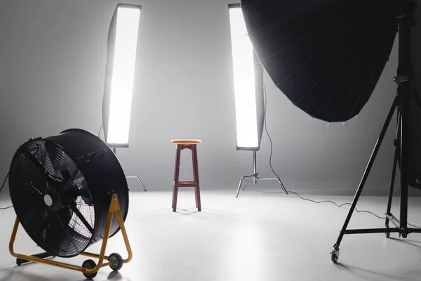 Digital camera, fan, reflector, wooden stool and lights on backstage in photo studio — Stock Photo