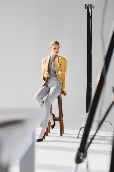 Selective focus of stylish model posing and sitting on stool on backstage — Stock Photo