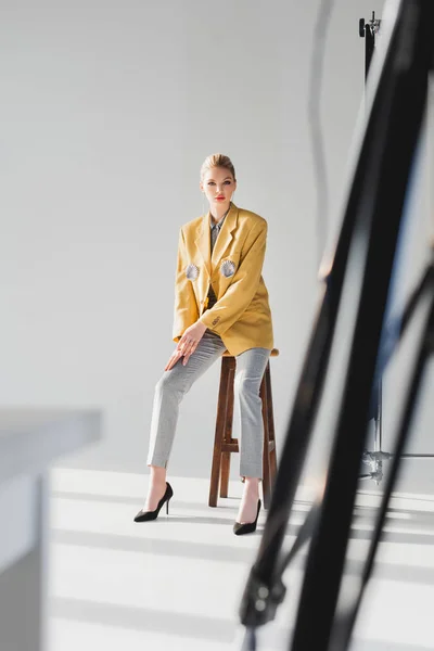 Selective focus of stylish model posing and sitting on stool on backstage — Stock Photo