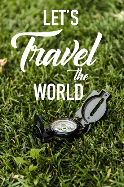 Selective focus of black vintage compass on green grass near lets travel the world letters — Stock Photo
