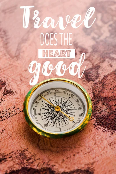 Top view of golden compass on map near travel does the heart good letters — Stock Photo