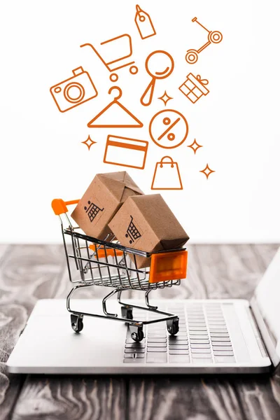 Selective focus of toy shopping cart with small carton boxes on laptop keyboard near illustration on white, e-commerce concept — Stock Photo