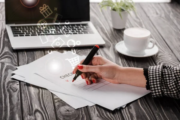 Vue recadrée d'une femme d'affaires tenant un stylo marqueur rouge près de la liste de contrôle, illustration, tasse et ordinateur portable sur la table, concept de commerce électronique — Photo de stock