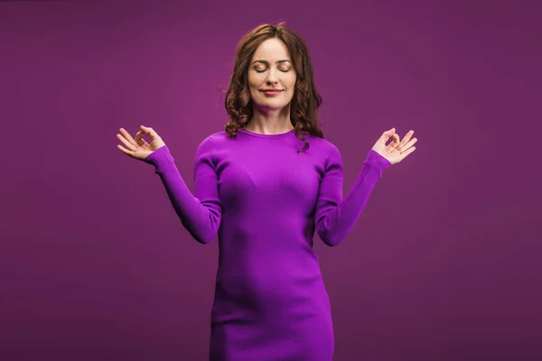 Mujer positiva meditando con los ojos cerrados sobre fondo púrpura - foto de stock