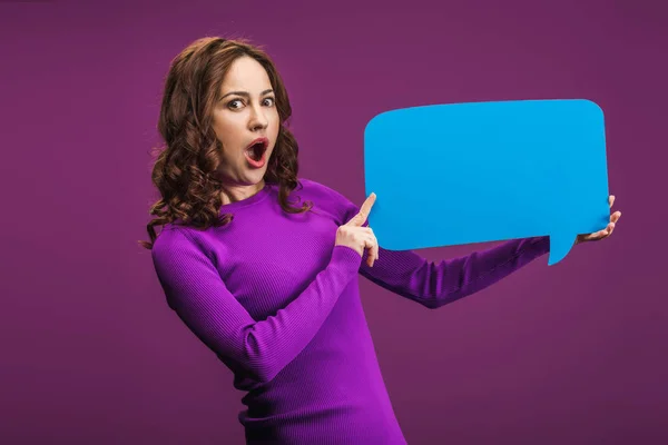 Mujer conmocionada sosteniendo la burbuja del discurso sobre fondo púrpura - foto de stock