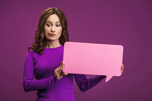 Skeptical woman holding speech bubble on purple background — Stock Photo