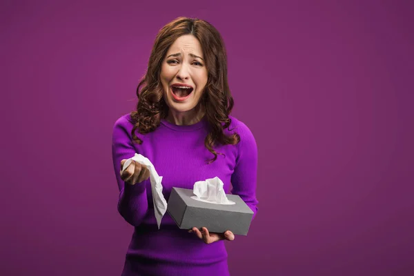 Triste mulher chorando enquanto segurava guardanapos de papel no fundo roxo — Fotografia de Stock