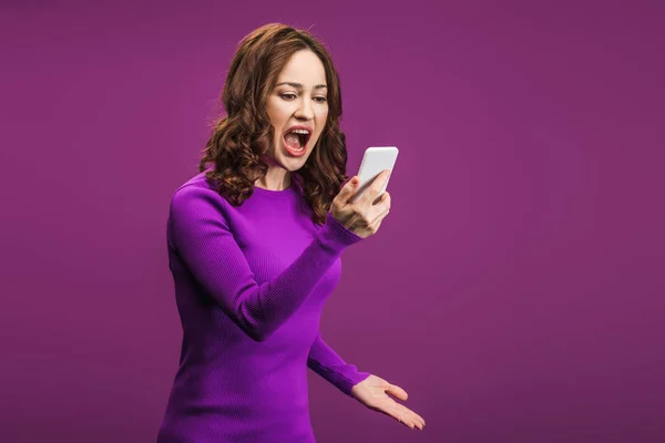 Irritated woman looking at smartphone during video call on purple background — Stock Photo