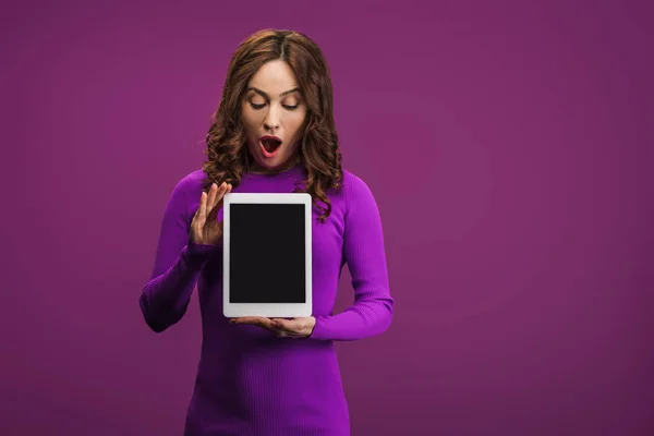 Шокированная женщина держит цифровой планшет с чистым экраном на фиолетовом фоне — стоковое фото