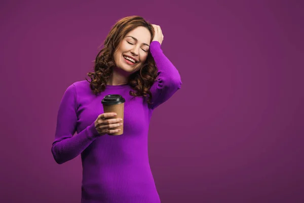 Ridere ragazza toccare la testa mentre tiene il caffè per andare su sfondo viola — Foto stock