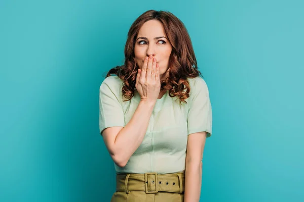Shocked girl looking away and covering mouth with hand on blue background — Stock Photo
