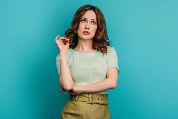 Dreamy woman looking up and touching hair while standing on blue background — Stock Photo