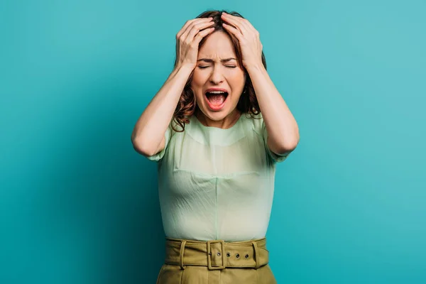 Femme en colère criant et tenant la main sur la tête sur fond bleu — Photo de stock