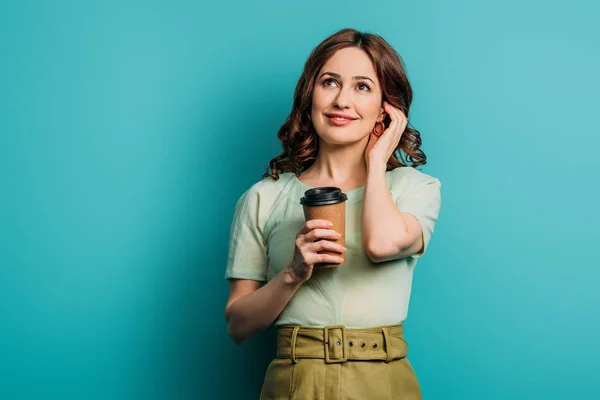 Chica de ensueño mirando hacia arriba mientras sostiene el café para ir sobre fondo azul - foto de stock