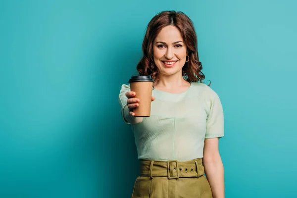 Attrayant, femme souriante montrant tasse en papier sur fond bleu — Photo de stock