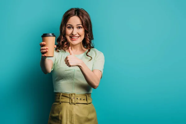Fröhliches Mädchen zeigt den Daumen nach oben, während es Kaffee hält, um auf blauem Hintergrund zu gehen — Stockfoto
