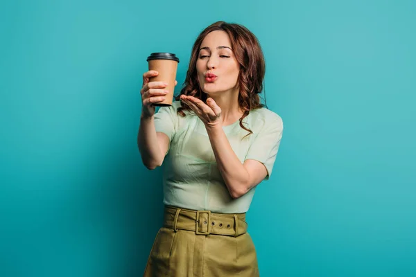 Positive Mädchen bläst Luftkuss, während sie Kaffee halten, um auf blauem Hintergrund zu gehen — Stockfoto