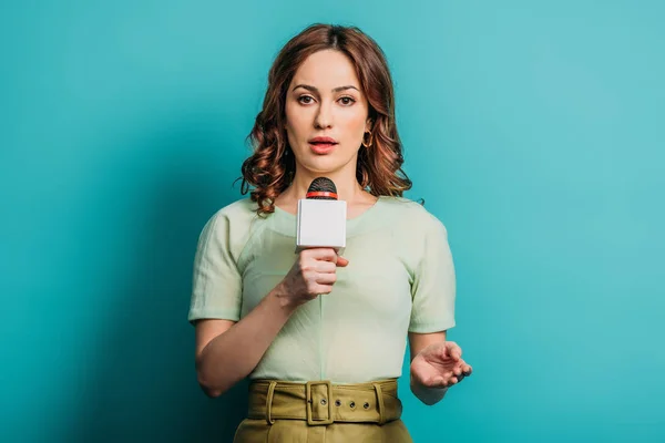 Serious journalist looking at camera while holding microphone on blue background — Stock Photo