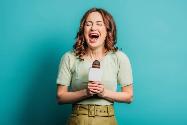 Jornalista alegre rindo enquanto segurando microfone no fundo azul — Fotografia de Stock